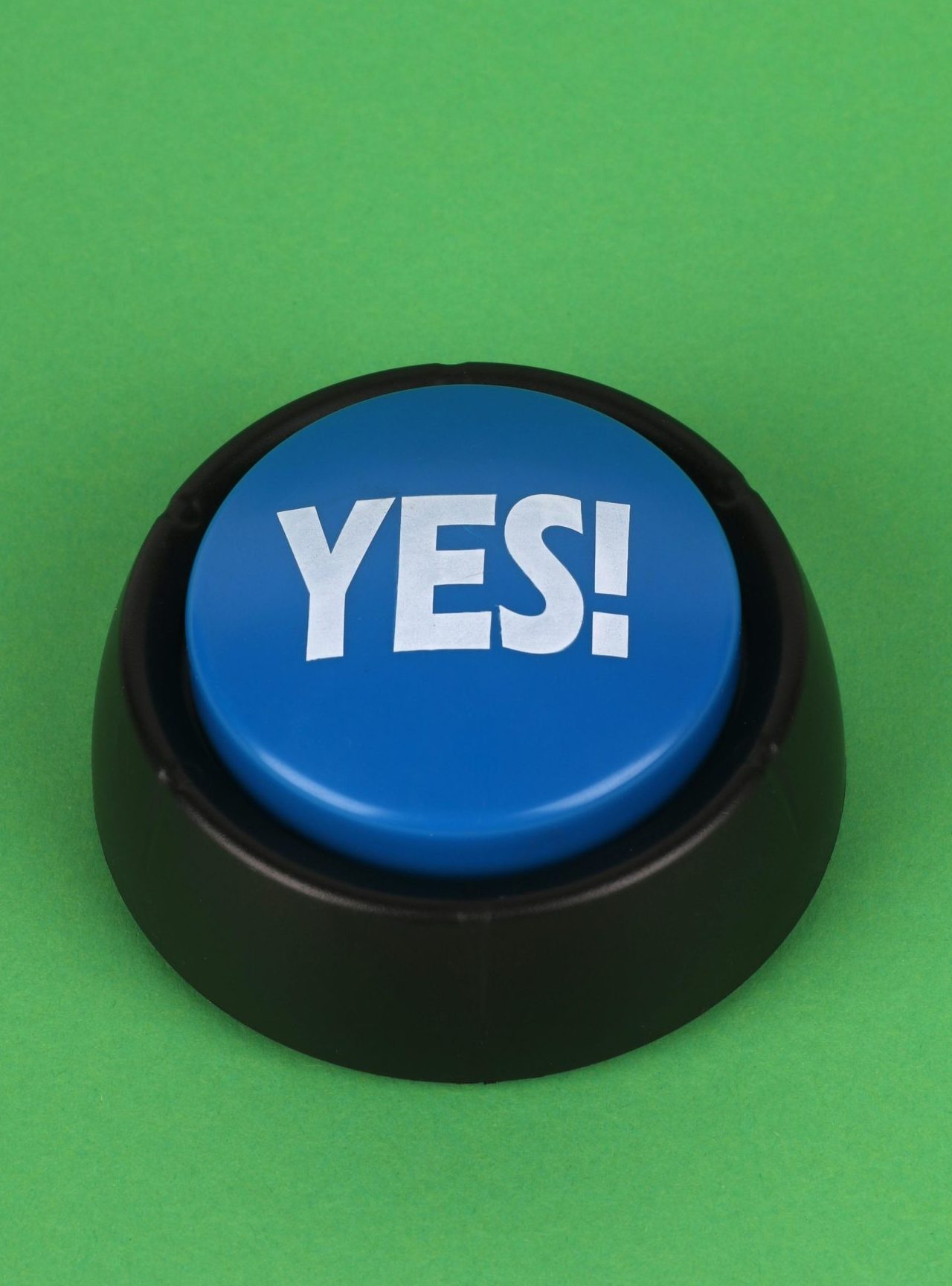 Photo of a blue button with 'YES!' text on a green background in a vertical composition.