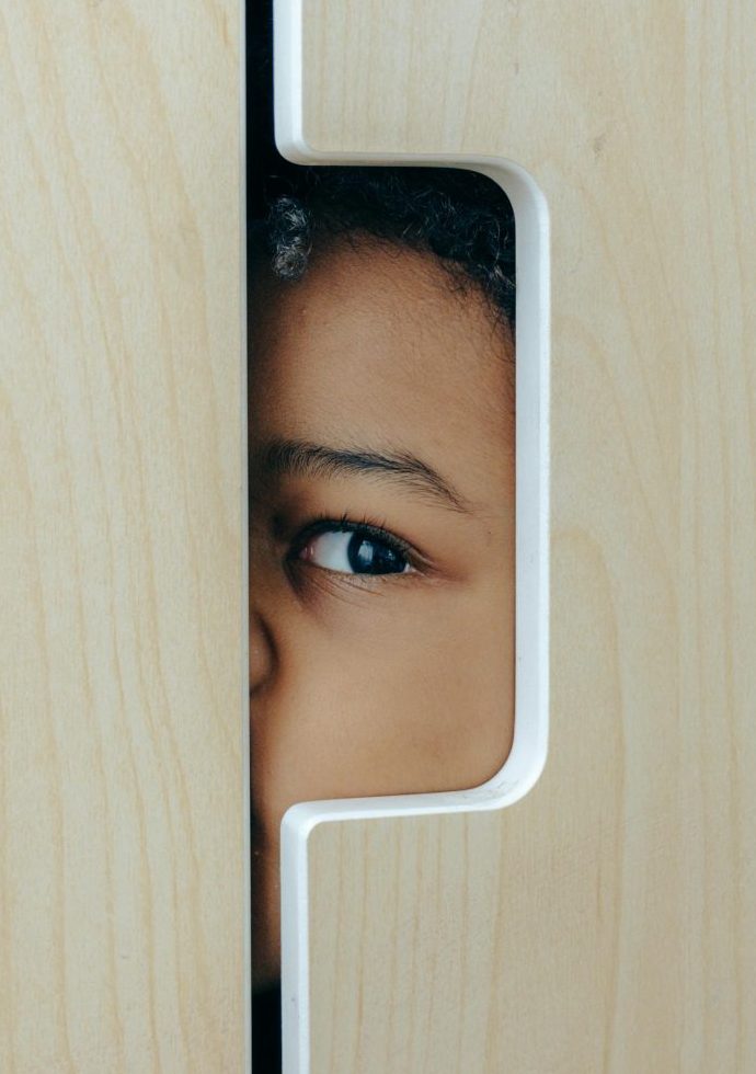 A child's curious eye peeking through a closet door indoors.